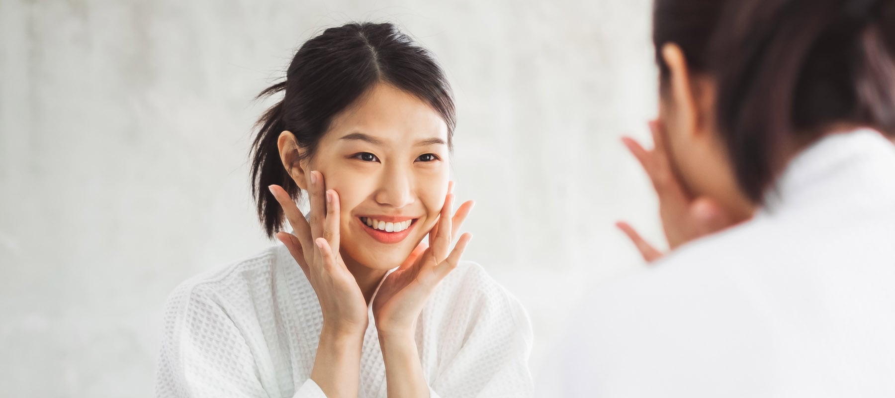 Jeune femme coréenne souriante commençant sa routine visage face au miroir
