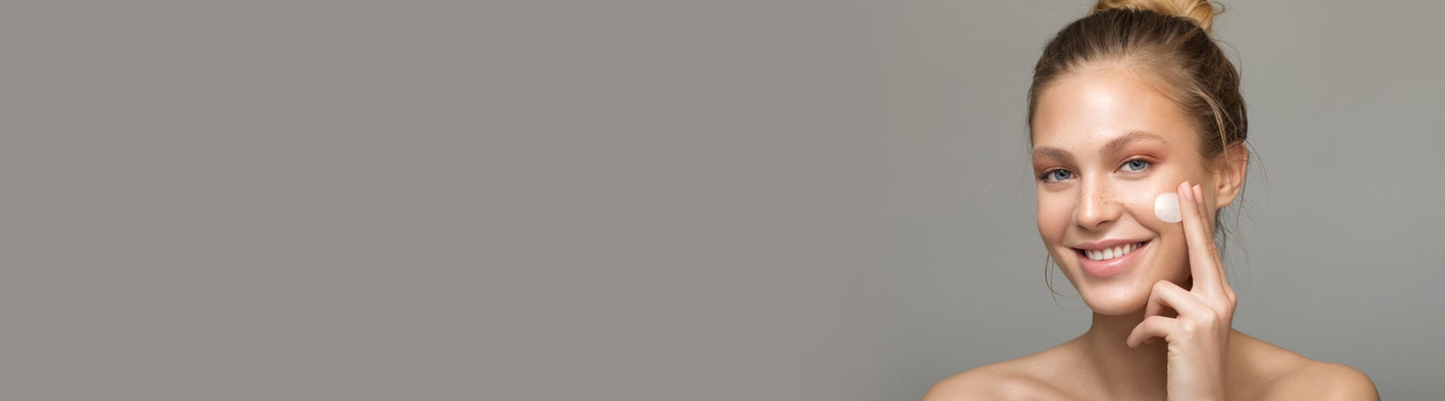 jeune femme souriante mettant de la crème hydratante sur le visage