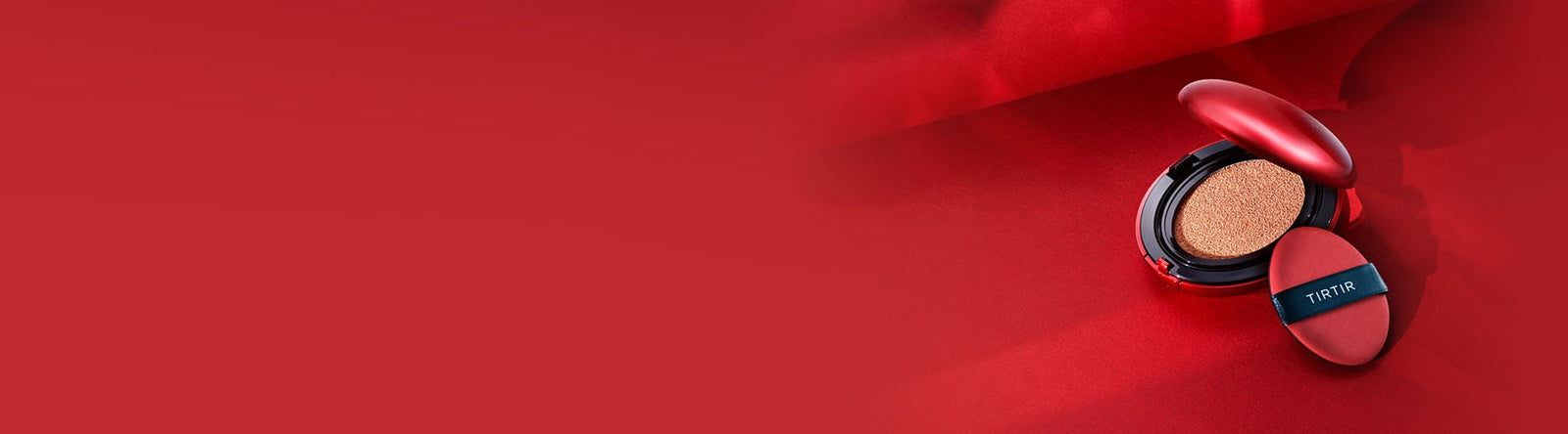 Un fond de teint coussin compact rouge avec une houppette applicatrice étiquetée TIRTIR est ouvert sur un fond en tissu rouge, avec un grand espace rouge vide sur le côté gauche.