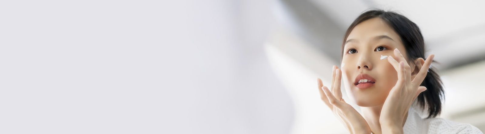 Jeune femme coréenne se mettant de la crème hydratante face à son miroir