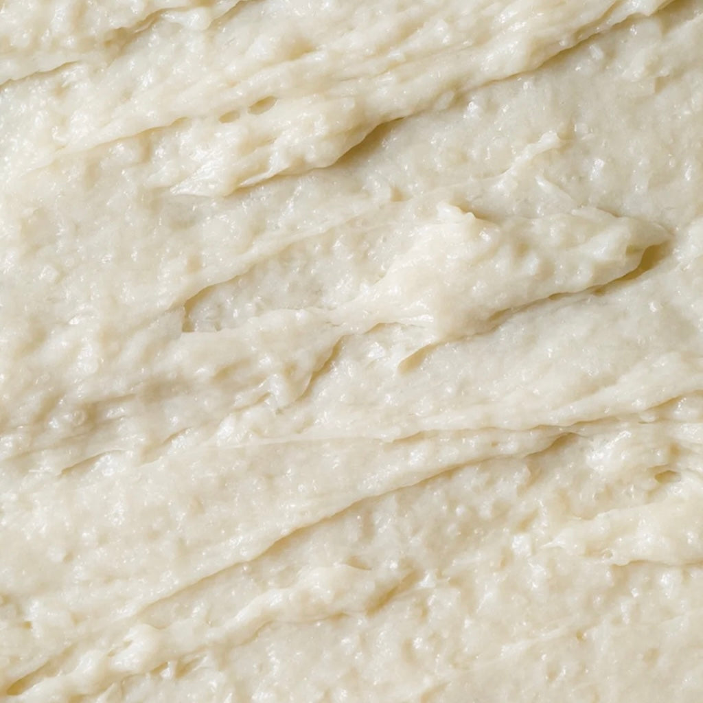 Zoom macro sur la texture exfoliante du scrub BEIGIC, montrant les grains fins de sel marin infusés d'extraits de café vert, prêts à fondre en mousse.