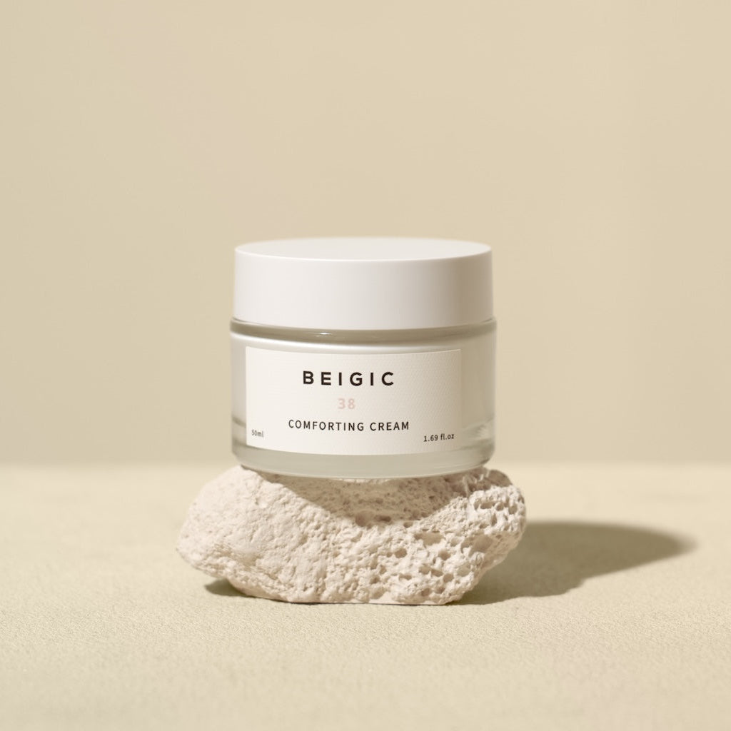 Le pot de crème BEIGIC posé sur un linge en coton blanc à côté de fleurs de camomille, capturant une atmosphère épurée, lumineuse et réconfortante.